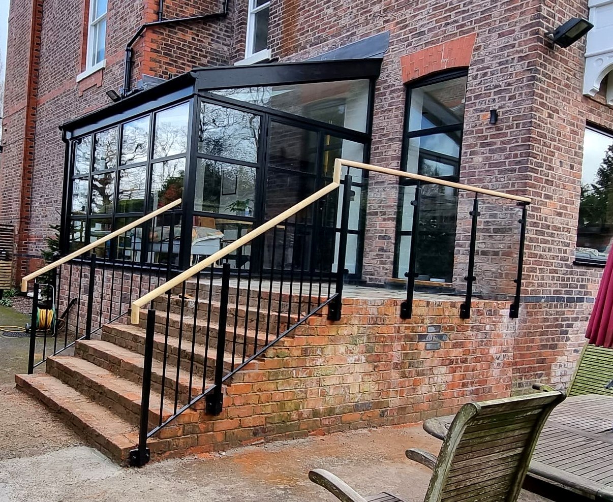 Powder-coated steel and glass balustrade with an iroko handrail to a raised terrace, Timperley, South Manchester
